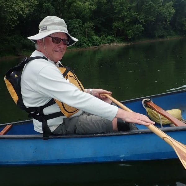 A man in a hat and sunglasses paddling a canoe.
