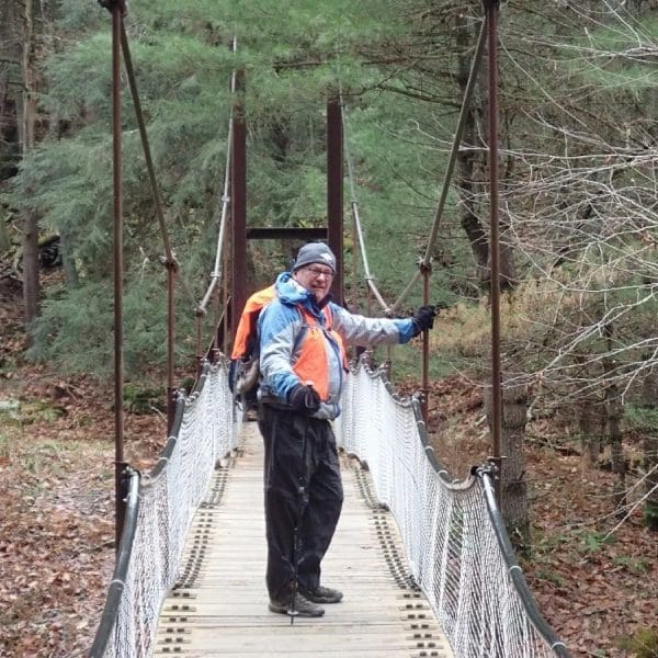 A man on a suspension bridge in the woods.