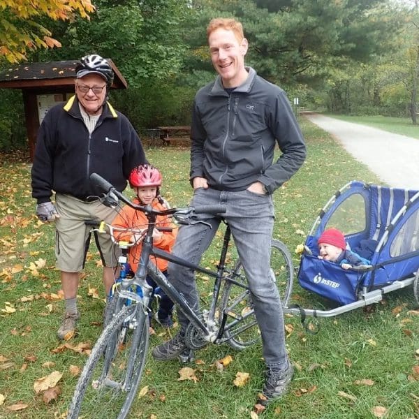 Two men standing next to a bicycle and trailer.